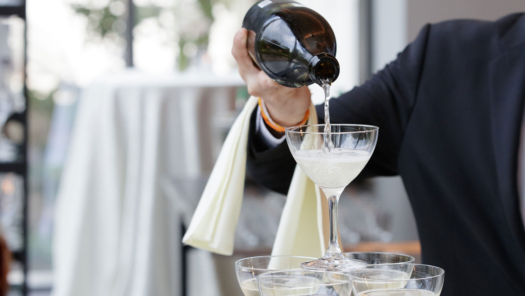 Champagne being poured over glasses stacked in a tower formation. 