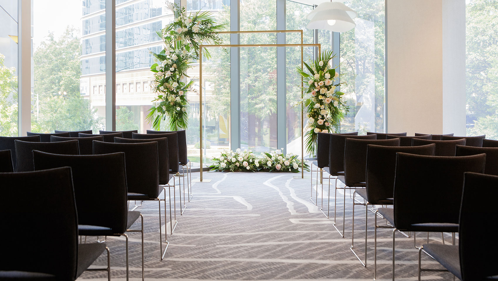 Wedding ceremony set up in our Venture ballroom, an arch with delicately placed flowers and black chairs lining the aisle