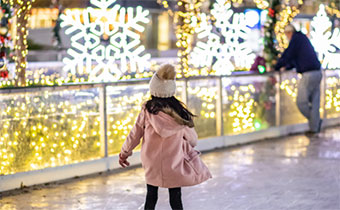 Little girl ice skating with holiday lights