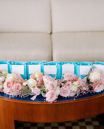 Wedding welcome bags set out on a coffee table, surrounded by pink flowers